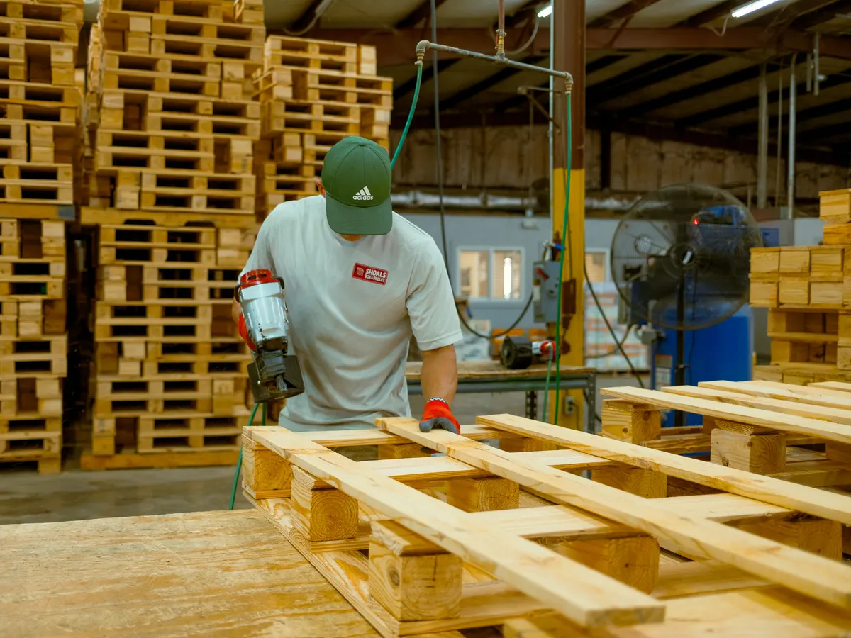 A Shoals Box & Pallet employee nailing deck boards onto a new wooden pallet