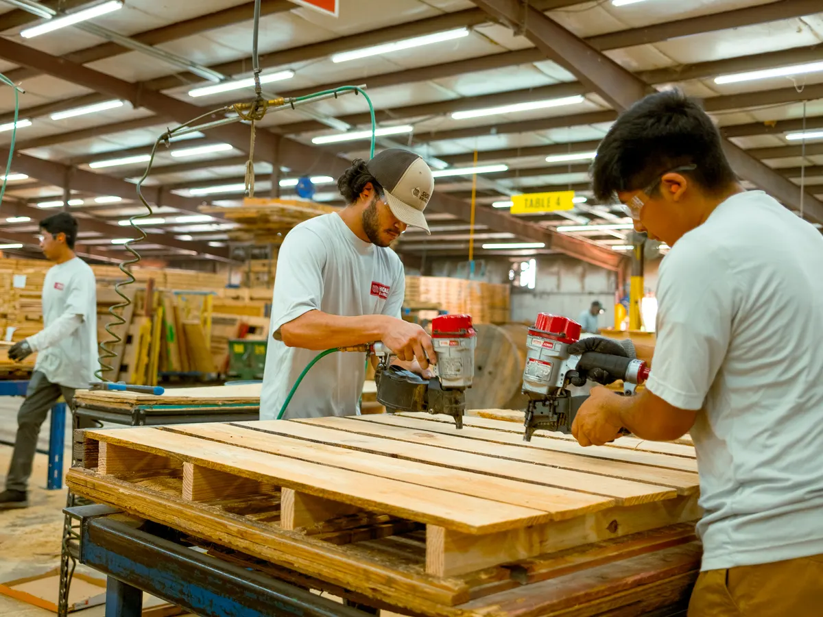 Two Shoals Box & Pallet employees assembling a wooden pallet with pneumatic nailers at the Florence plant