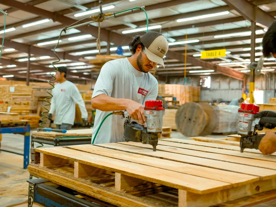 An employee running a pneumatic nailer along the deck boards of a pallet