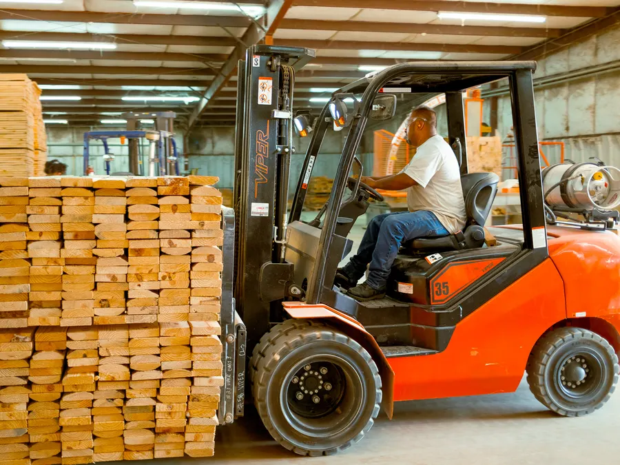 An operator moving a stack of cut lumber with a forklift inside the plant